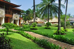 A tropical resort with a well-maintained garden, palm trees, and traditional architecture.