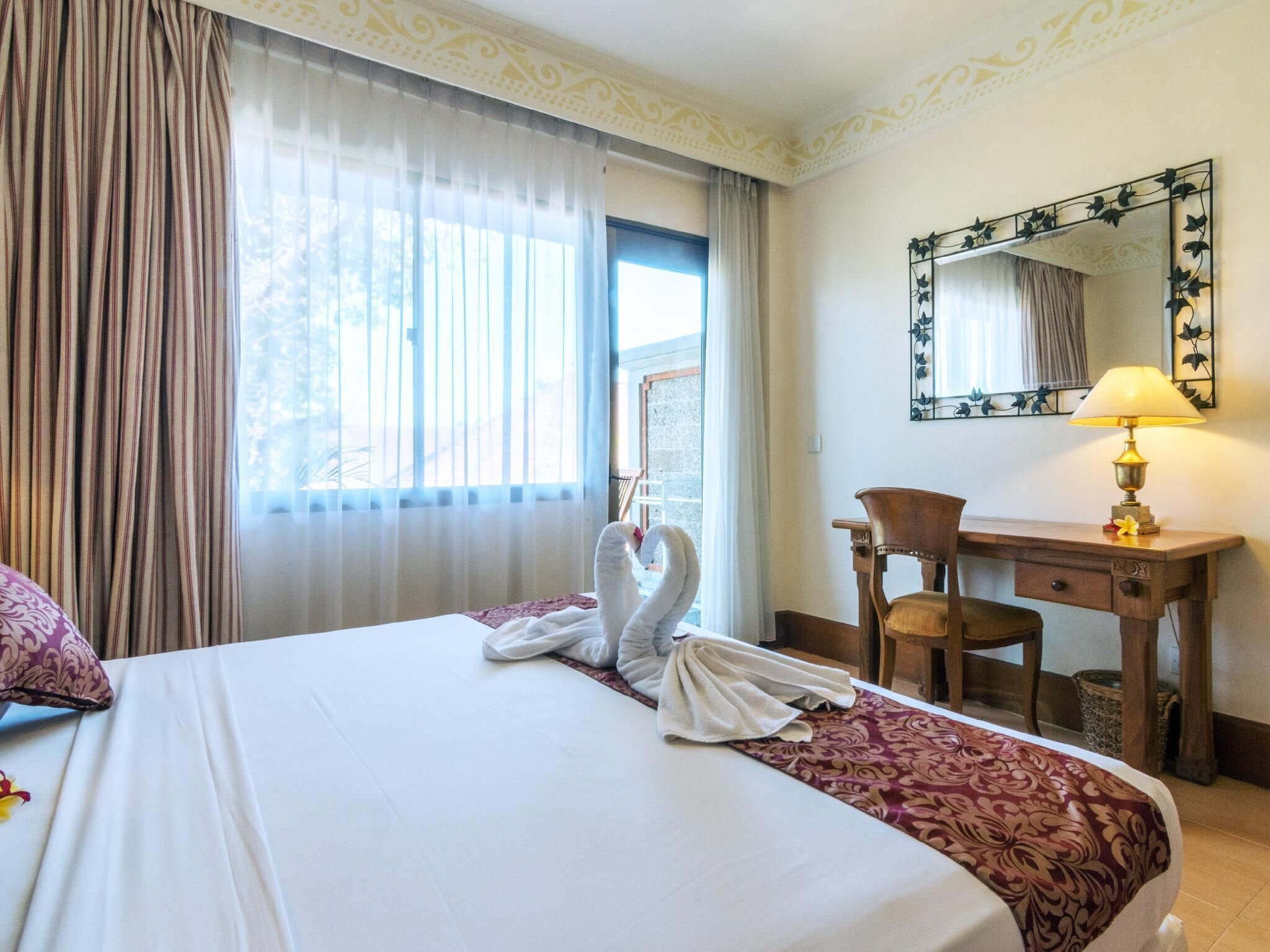 A hotel room with a bed, a desk, a chair, a lamp, and a window with curtains.