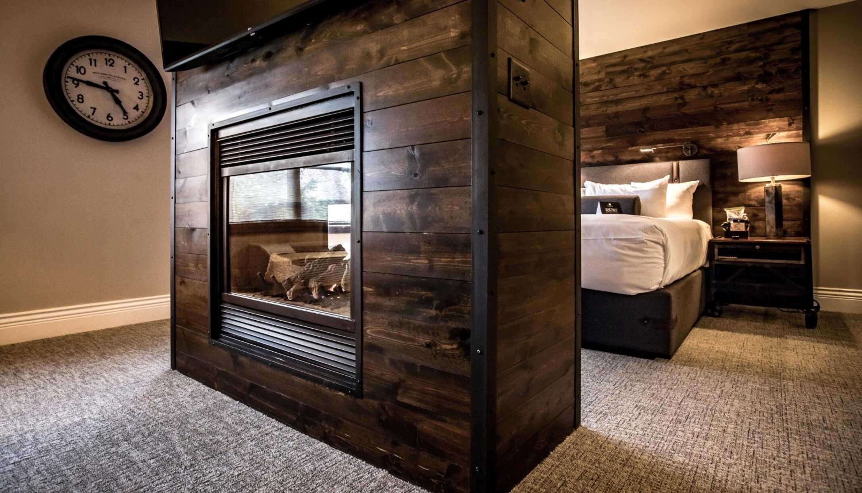 A cozy room with a fireplace, a bed, a nightstand, and a clock on the wall.