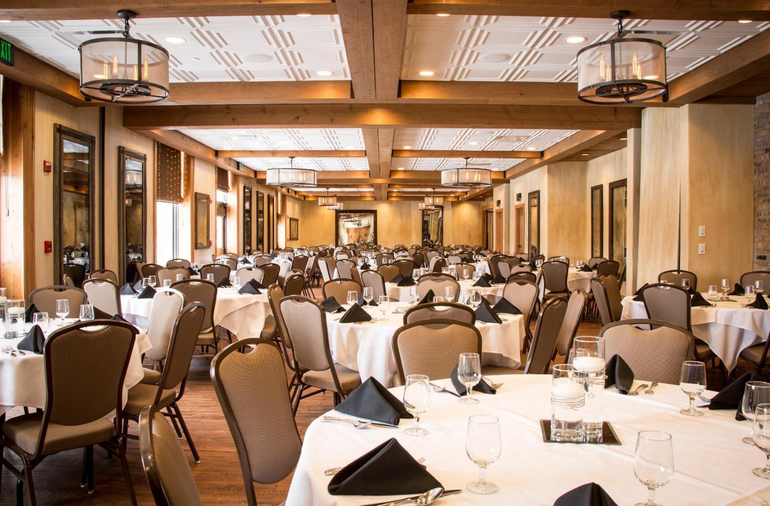 Une vaste salle de banquet avec de longues rangées de tables et de chaises, des poutres en bois au plafond et des lustres.
