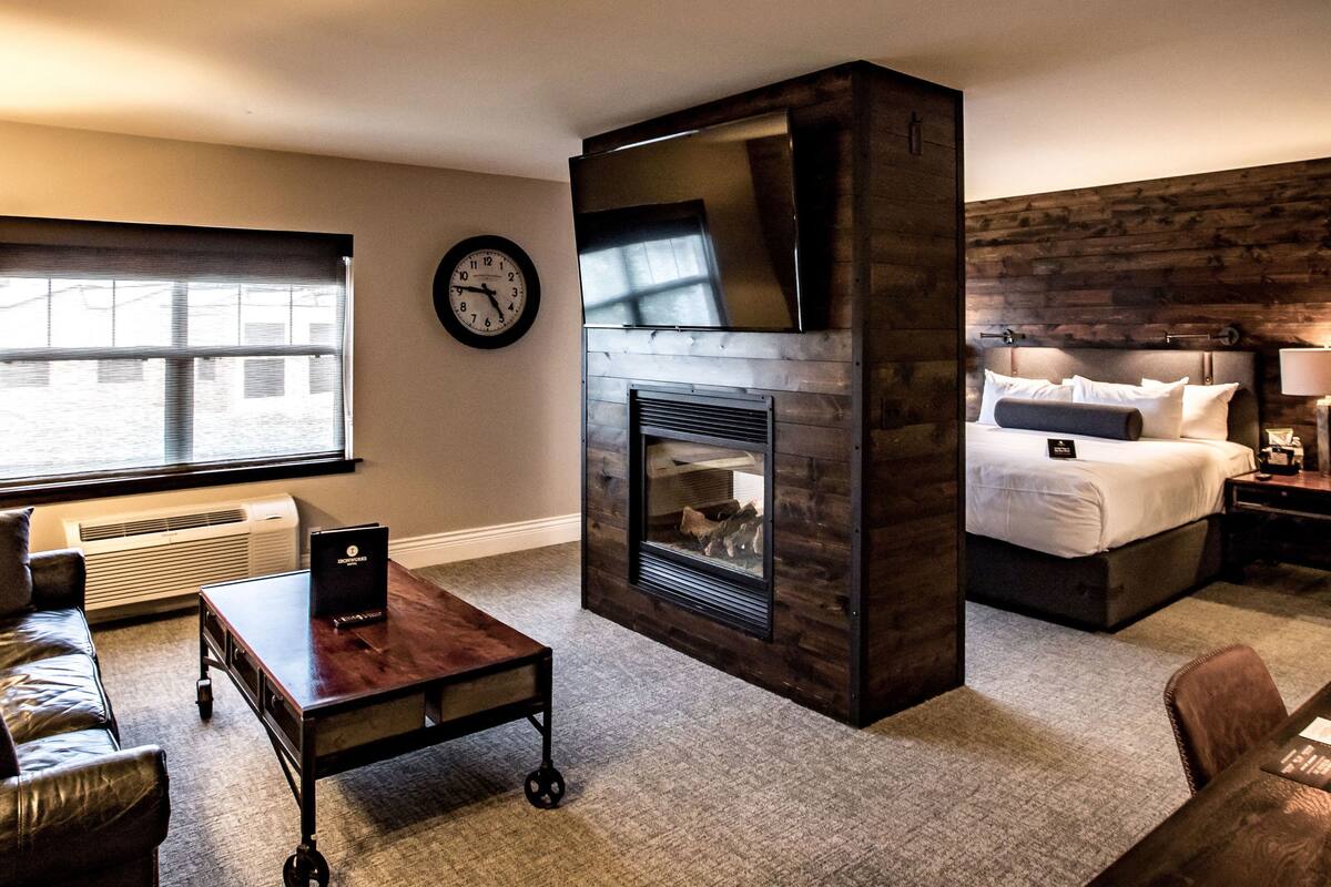 Ein Hotelzimmer mit Kamin, einem Bett, einem Schreibtisch, einem Ledersofa und einem großen Fenster.