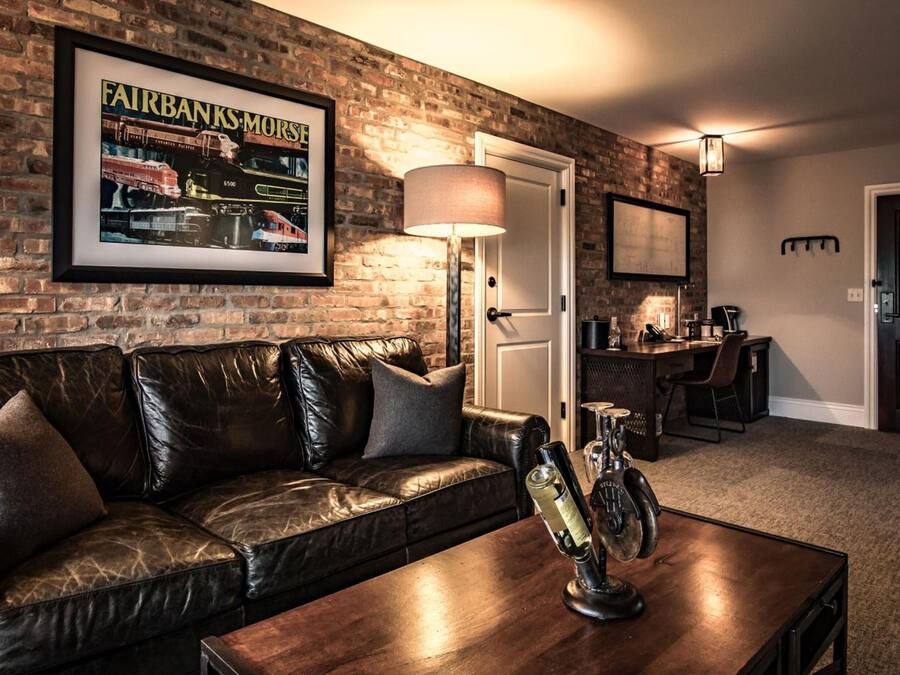 Una sala de estar con pared de ladrillo, una revista enmarcada, un sofá de cuero, una mesa de centro y una zona de bar con una lámpara.