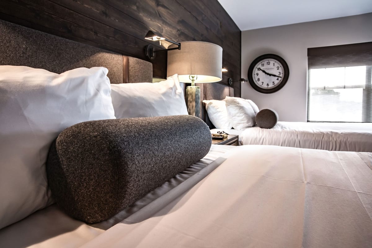 Ein modernes Hotelzimmer mit einem großen Bett, einem Nachttisch, einer Lampe und einer Wanduhr.