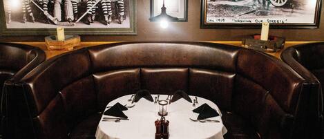 A dining area with a round table set for two, surrounded by leather booth seating.