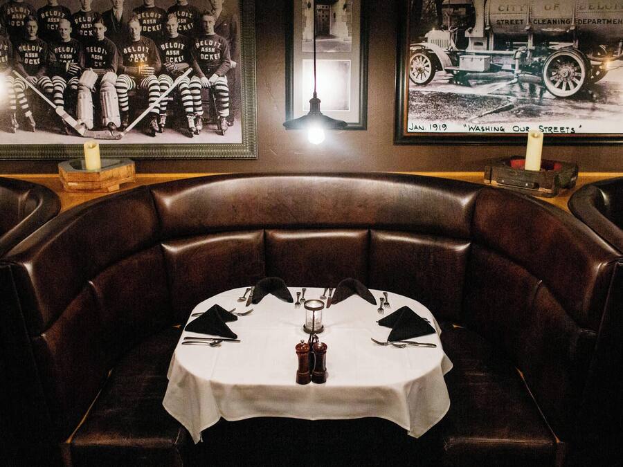 A dining area with a round table set for two, surrounded by leather booth seating.