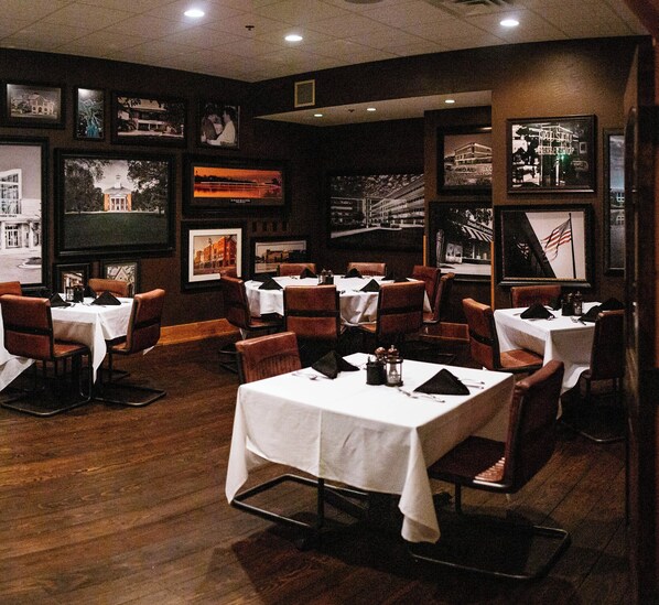 A restaurant with multiple tables and chairs, framed pictures on the walls, and a wooden floor.