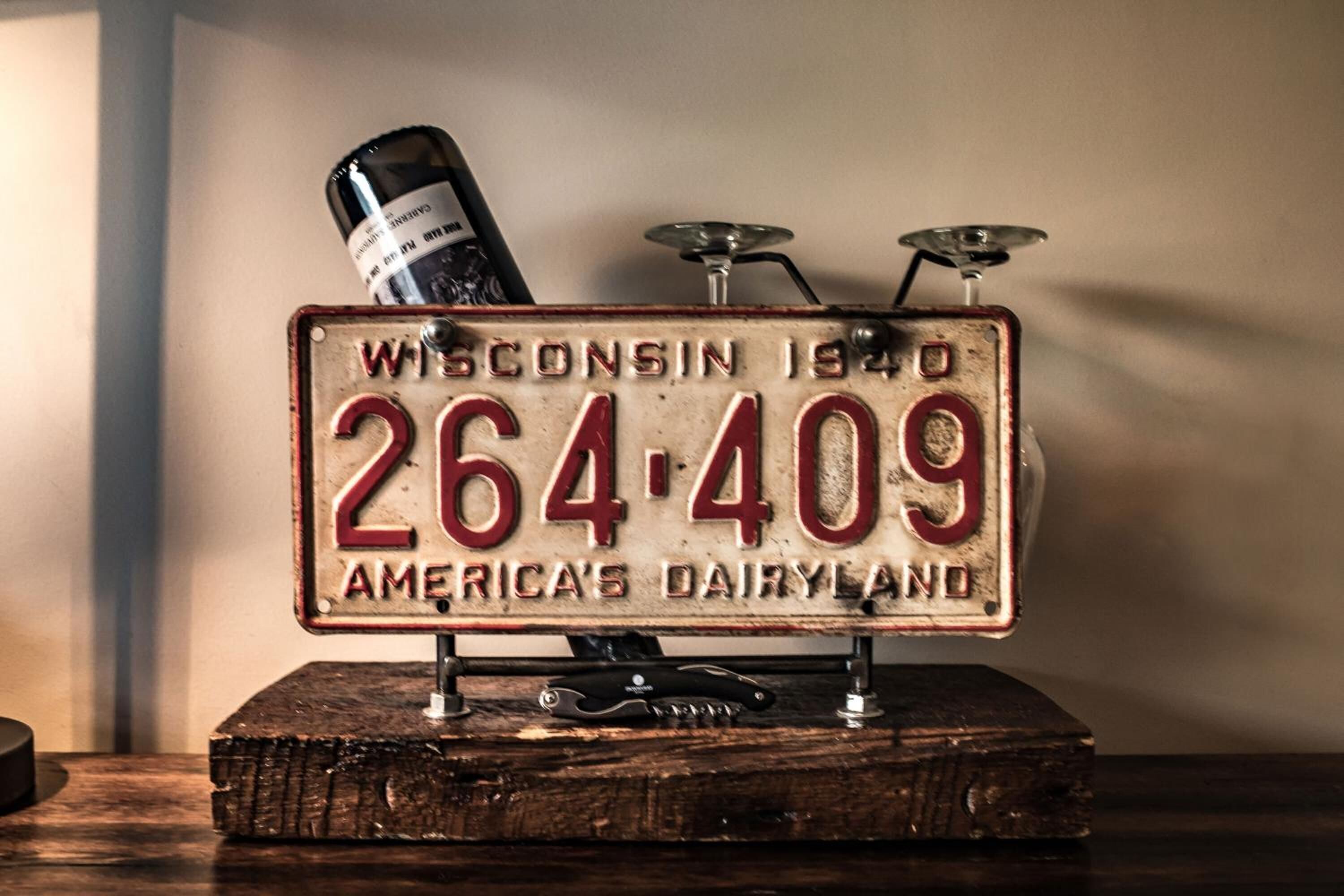 A vintage license plate with the text "Wisconsin 1940 264-409 America's Dairyland" mounted on a wooden base.
