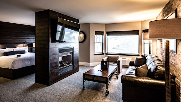 Una habitación de hotel moderna con cama, chimenea, sofá de cuero y un ventanal grande.