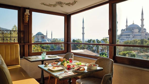 Un comedor con una mesa dispuesta para dos, un sofá y vistas a una mezquita con dos minaretes.