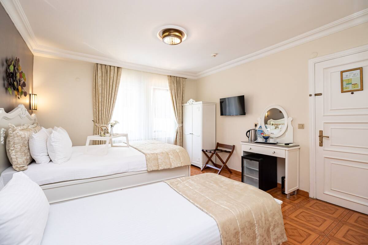 A hotel room with two beds, a desk, a television, a wardrobe, and a mirror.