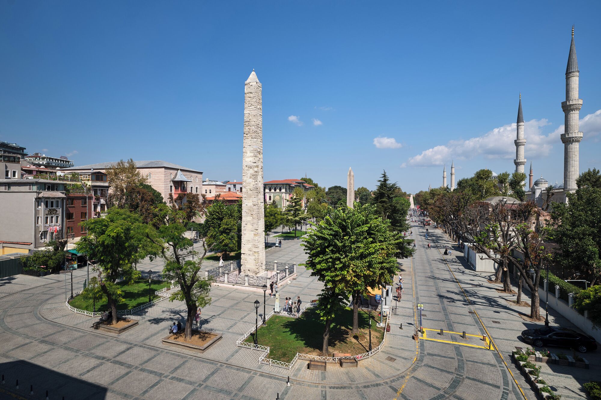 A square with a tall obelisk, trees, and a mosque with minarets.