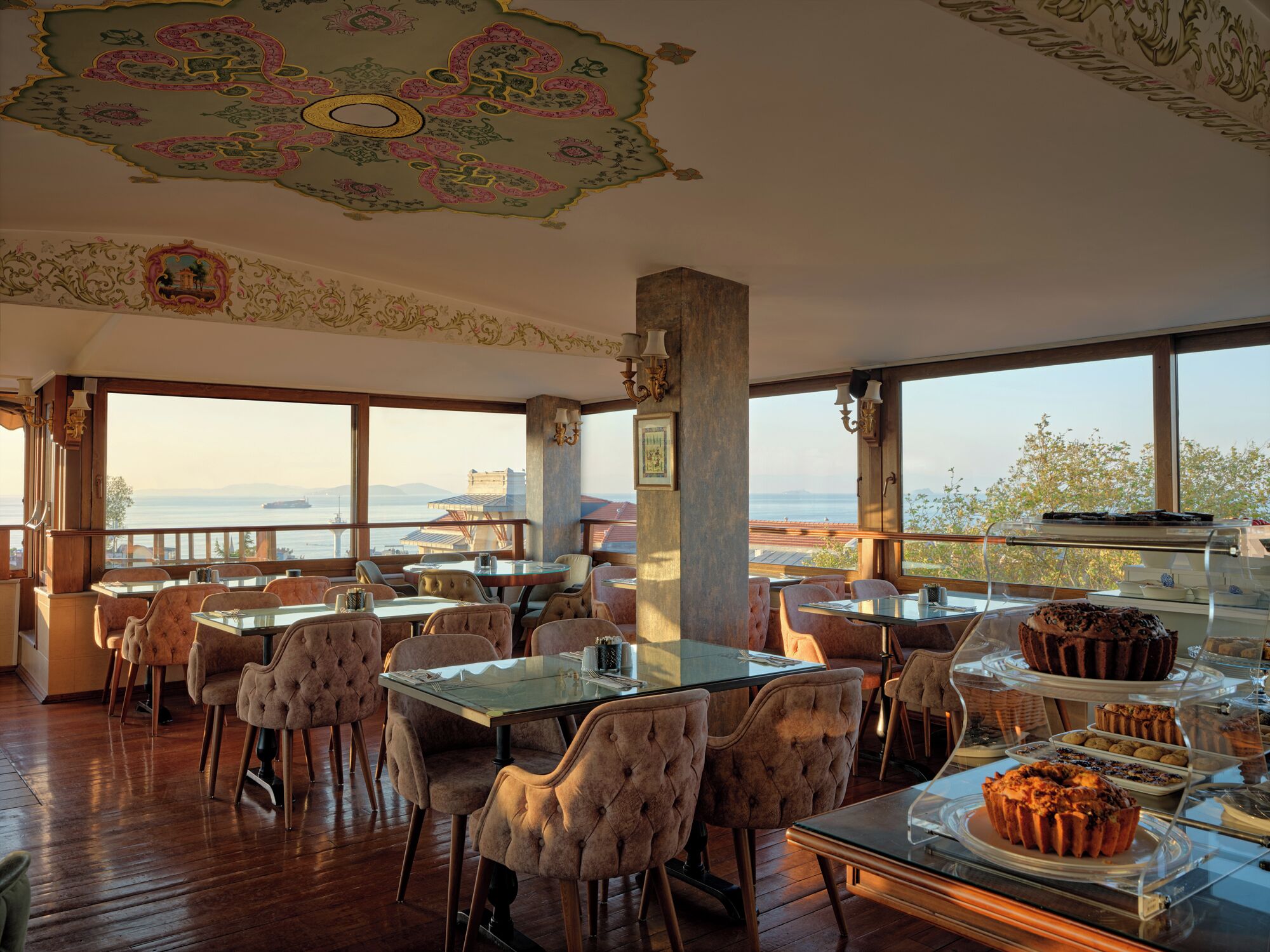 A restaurant with a view of the sea, featuring round tables and cushioned chairs.