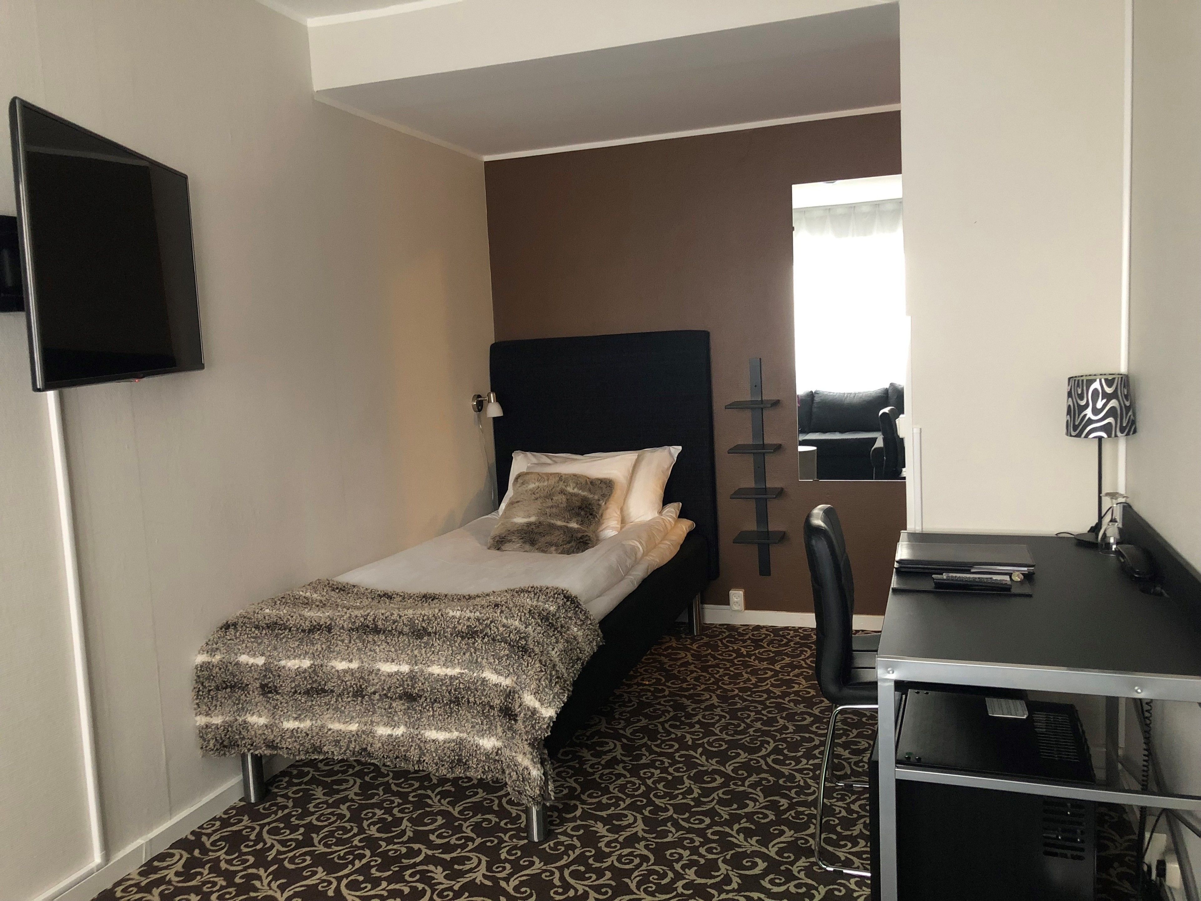 A small, neatly arranged bedroom with a bed, a desk, and a TV.