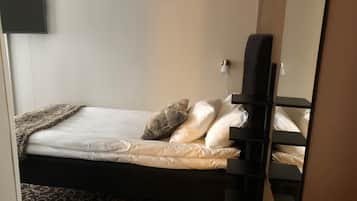Una cama individual con cabecera oscura, ropa de cama blanca y una alfombra estampada.