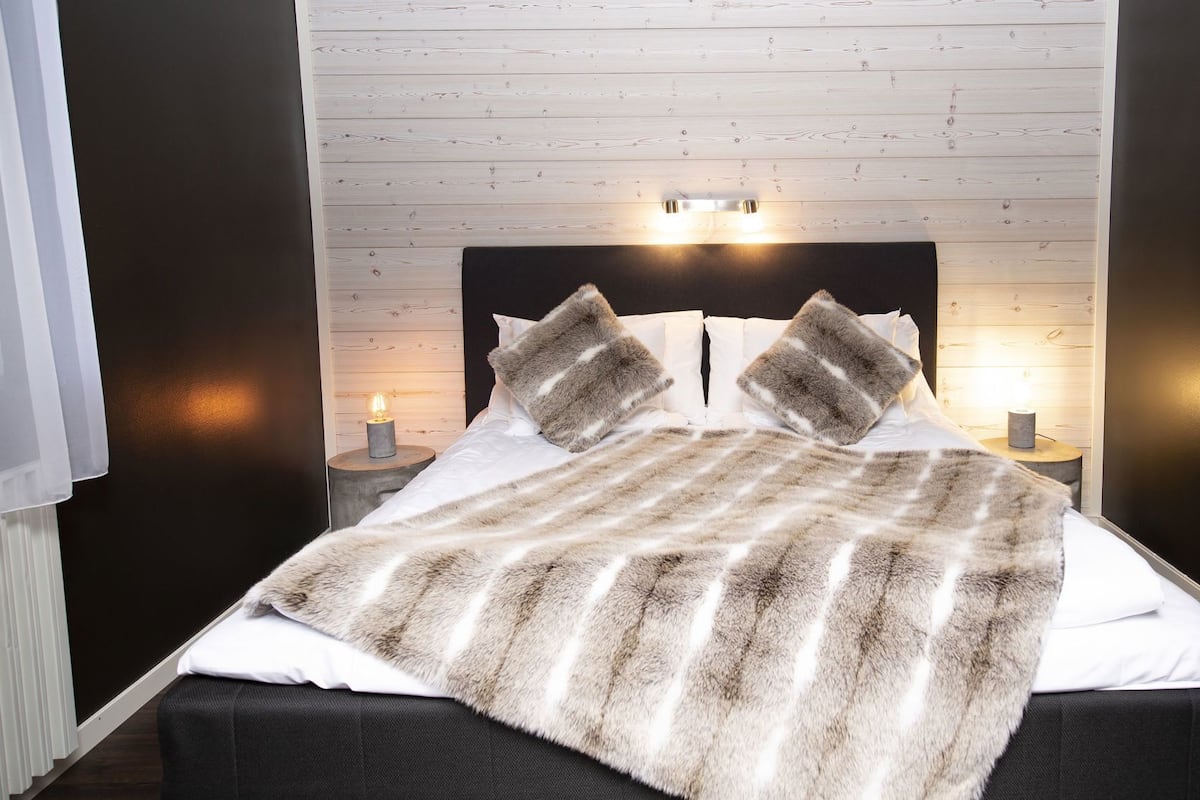 A bed with a fur throw, two bedside lamps, and a wooden headboard.