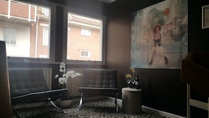 A room with a large window, a black leather chair, a small round table with a vase and wine bottle, and a painting on the wall. - Sure Hotel by Best Western Algen (Östersund)
