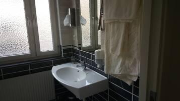 Un baño con un lavamanos blanco, paredes cubiertas de baldosas negras, una ventana y un perchero para toallas.