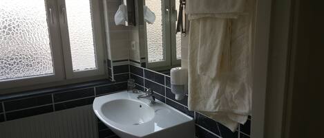 A bathroom with a white sink, black tiled walls, a window, and a towel rack.