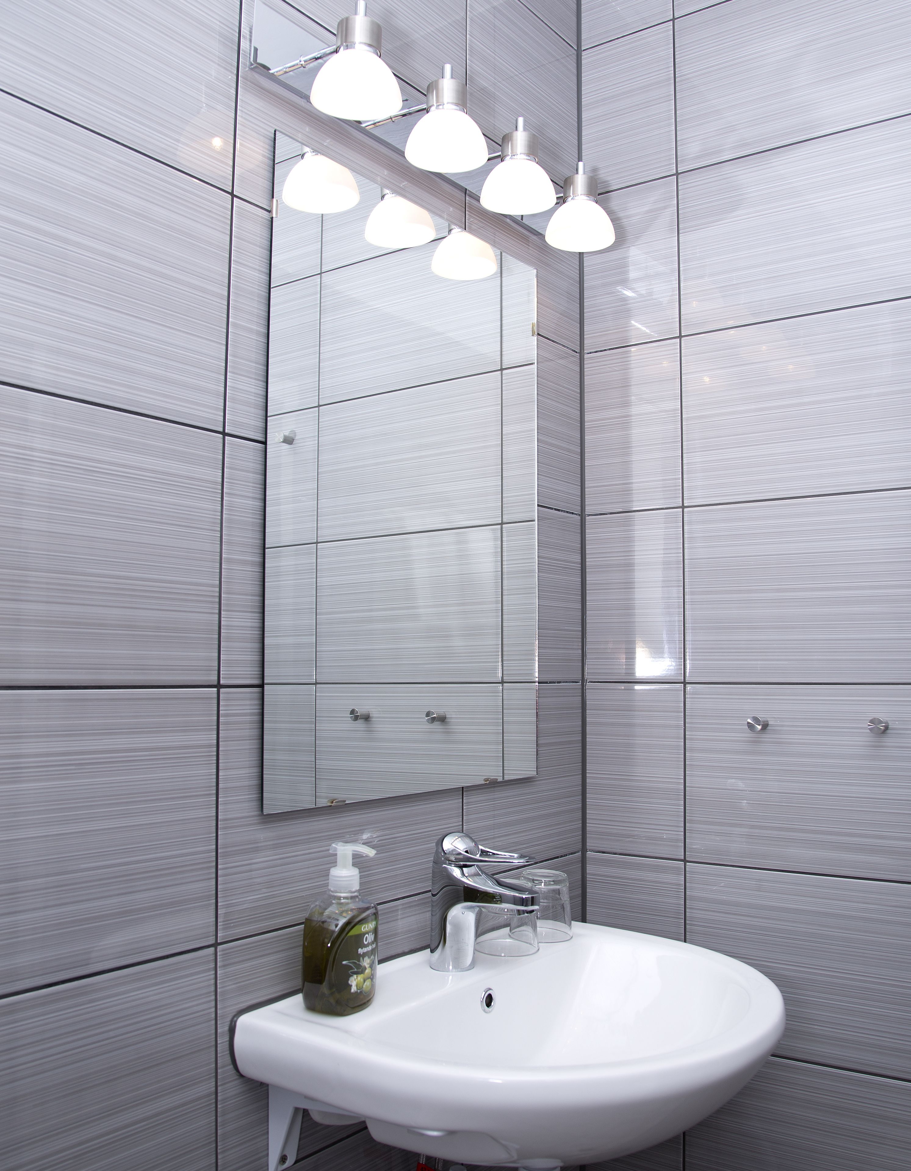 Une salle de bain moderne avec un grand miroir, un lavabo blanc et trois lampes suspendues.
