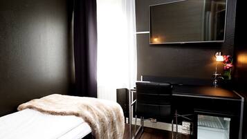 Ett hotellrum med en säng, ett skrivbord, en stol, en TV och ett litet kylskåp.