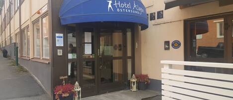 A hotel entrance with a blue awning, a glass door, and a sign indicating it is part of the Sweden Hotels chain.