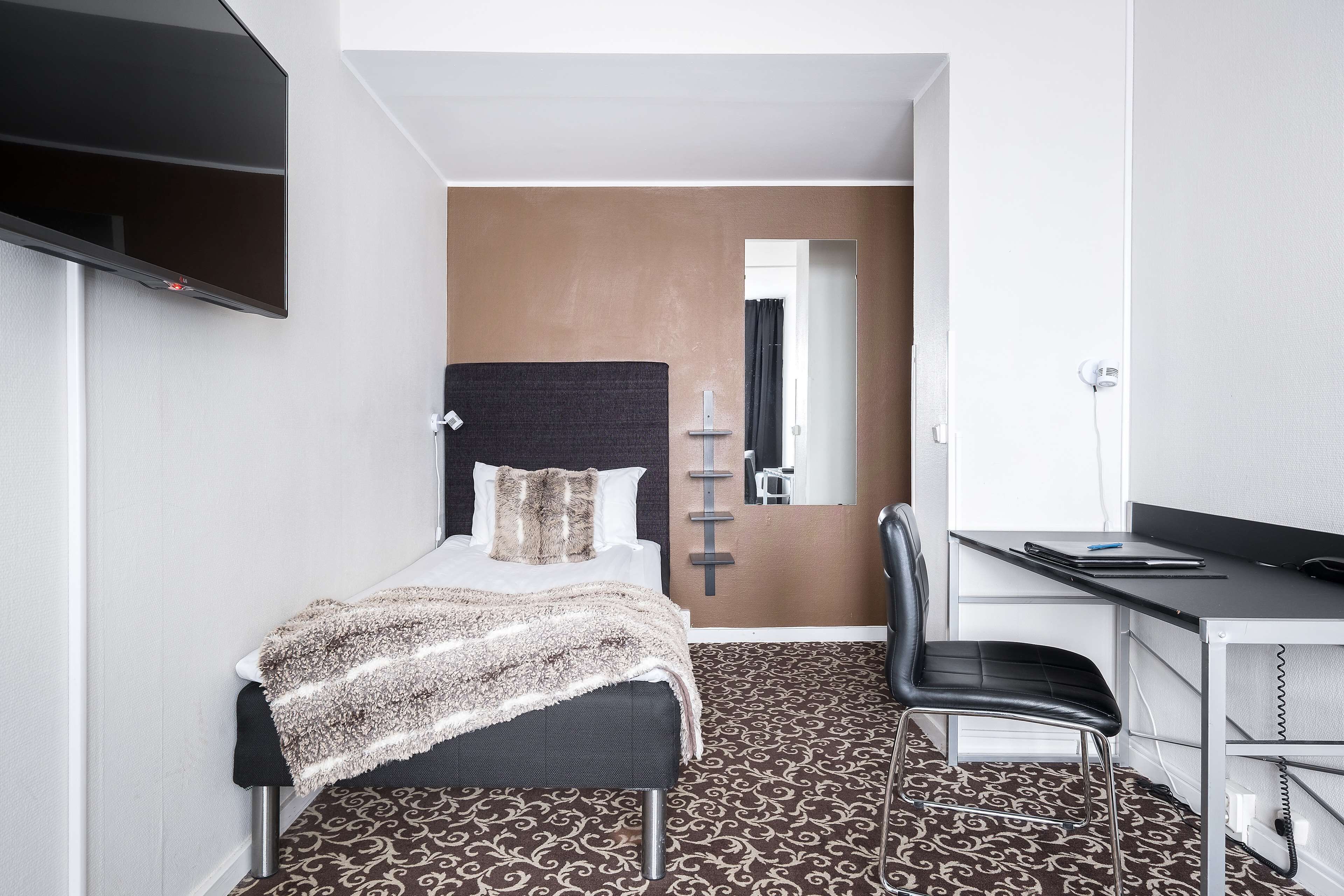 A compact hotel room with a bed, a desk, a chair, and a large mirror.