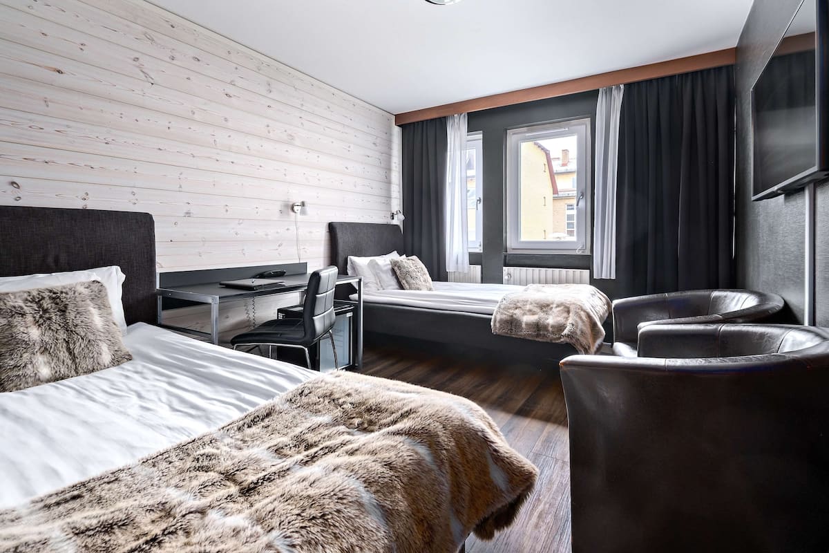 A hotel room with two beds, a desk, a chair, and a TV.