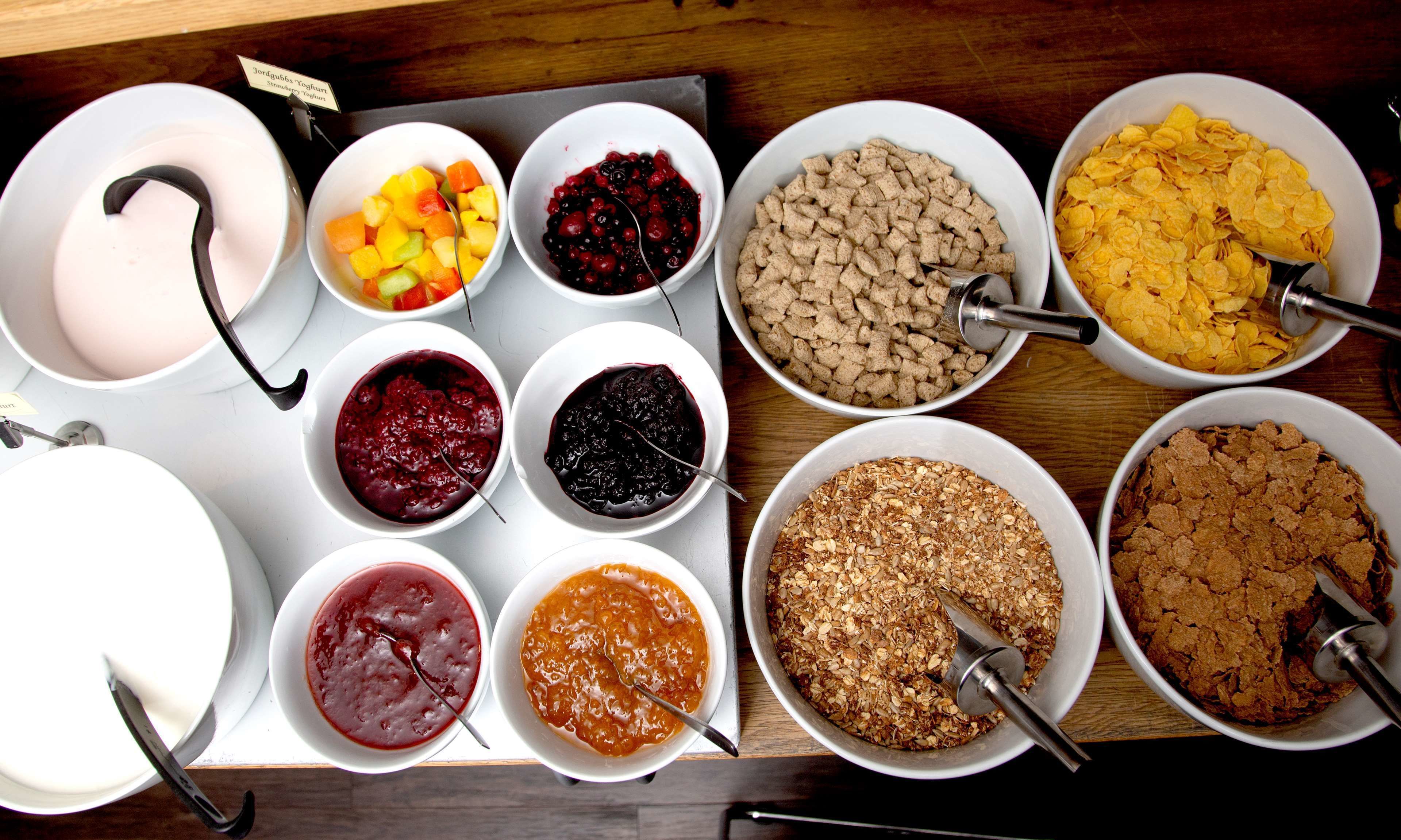 A variety of food items arranged on a tray, including bowls of yogurt, fruit, cereal, and oatmeal.
