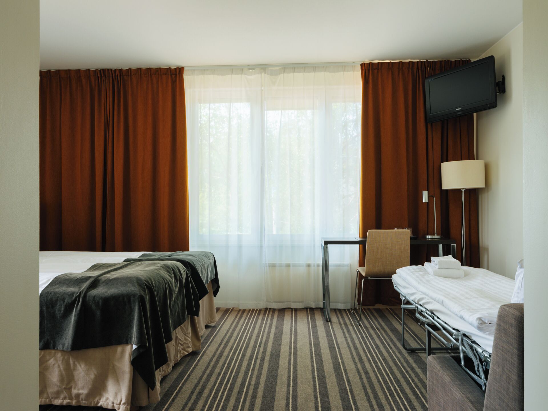 Habitación de hotel con dos camas, un escritorio, una silla, un televisor y una lámpara.