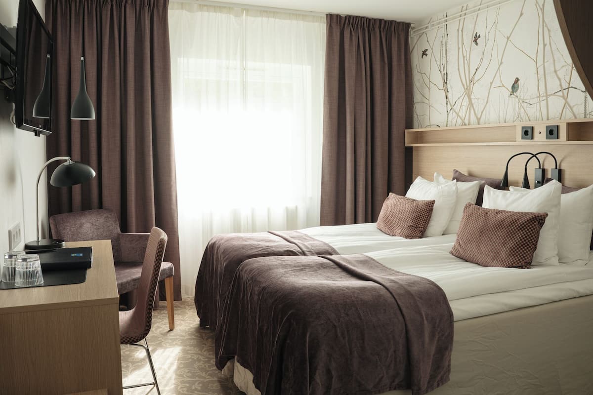 A hotel room with a bed, a desk, a chair, and a TV mounted on the wall.