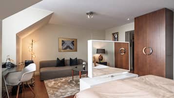 A modern hotel room with a bed, a desk with a chair, a sofa, a small table with a lamp, and a large mirror.