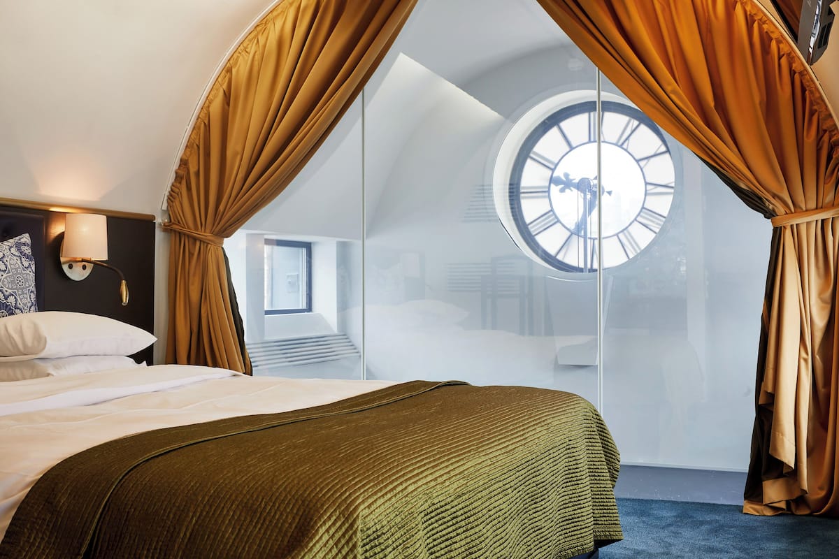A bedroom with a large bed, a window with curtains, and a clock on the wall.