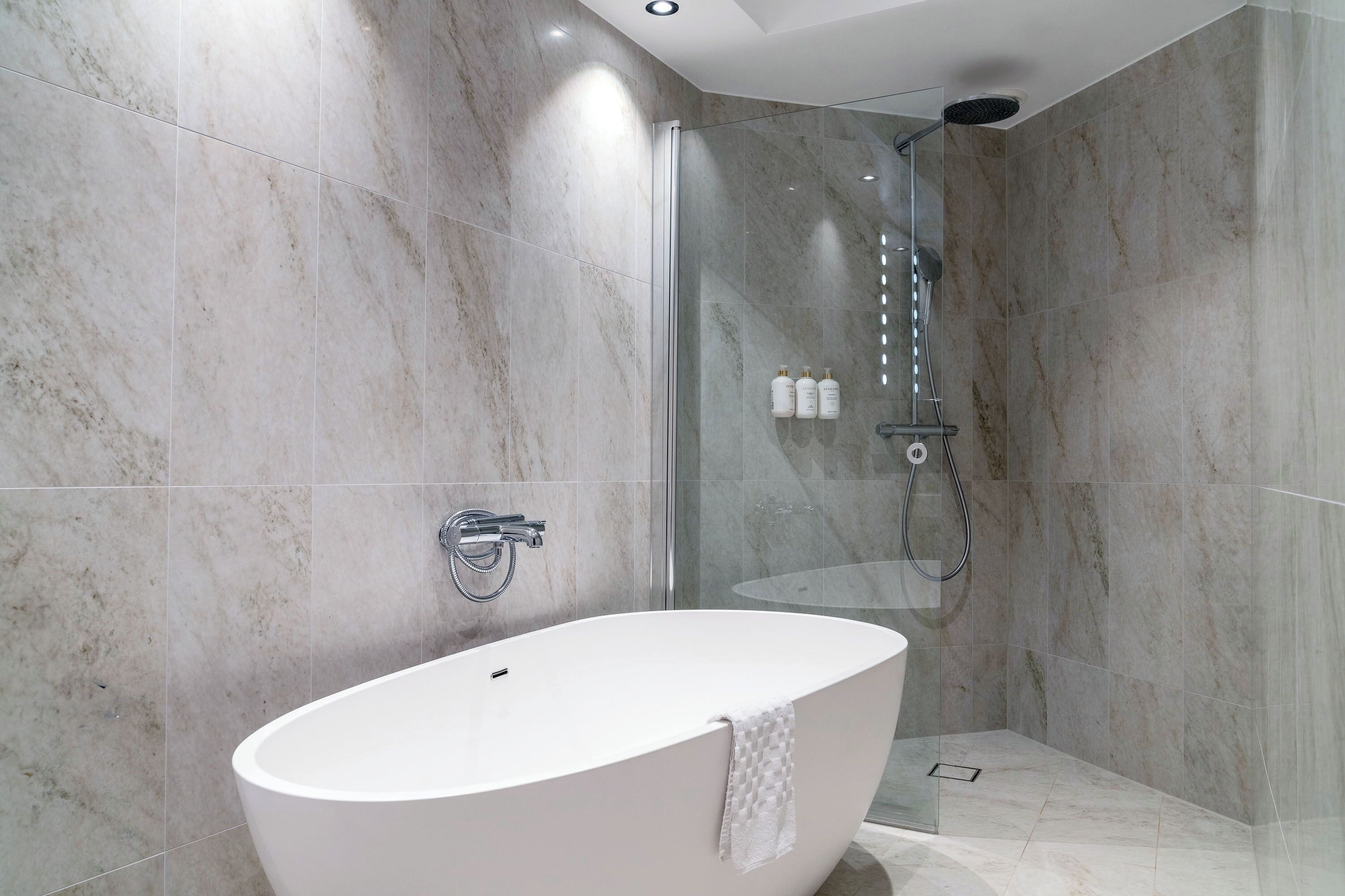 A modern bathroom with a freestanding bathtub, a glass-enclosed shower, and marble walls.