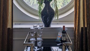 Une pièce dotée d’une grande fenêtre ornée d’un motif géométrique, d’un vase rempli de fleurs et d’une table sur laquelle se trouvent des verres et une bouteille.