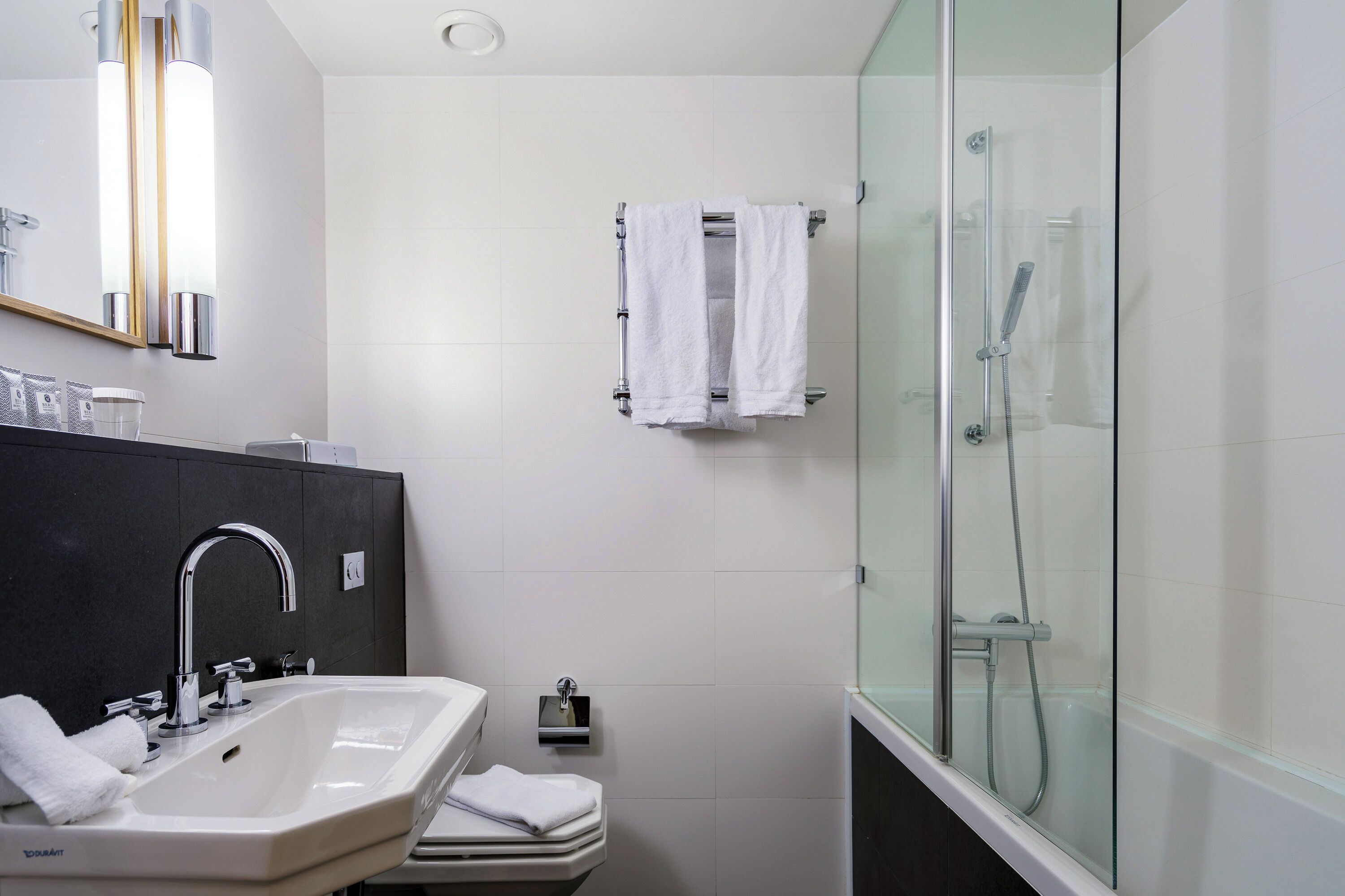 A modern bathroom with a large sink, a glass-enclosed shower, and a towel rack.