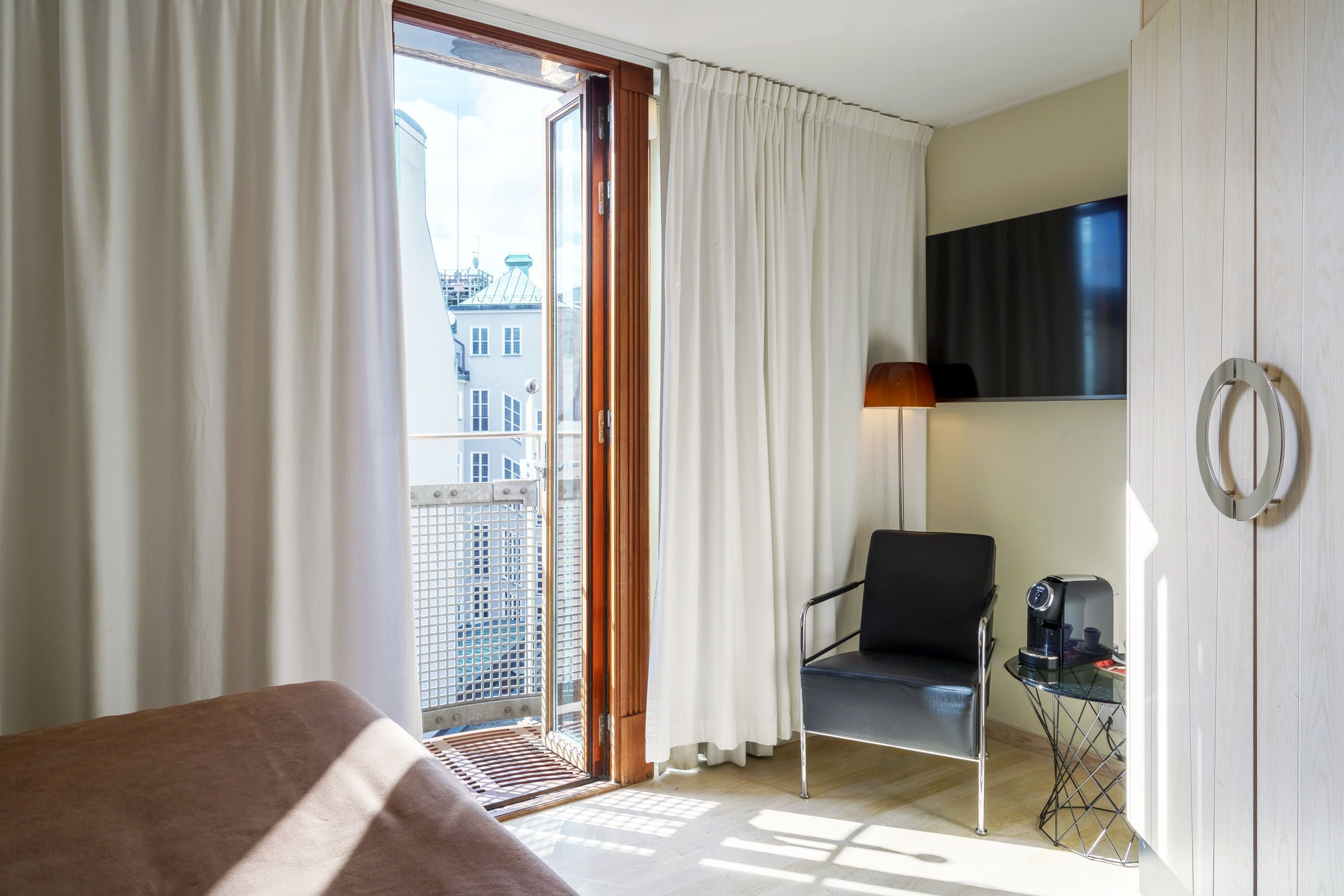 Une chambre d’hôtel avec un lit, une chaise, une petite table avec une machine à café, une télévision et une vue sur la ville par une grande fenêtre.
