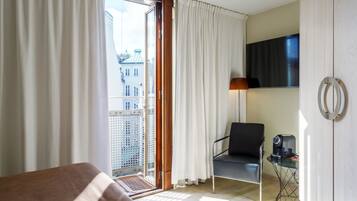 Une chambre d’hôtel avec un lit, une chaise, une petite table avec une machine à café, une télévision et une vue sur la ville par une grande fenêtre.