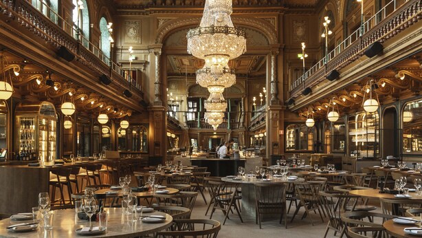 Une salle à manger spacieuse et élégante, dotée de nombreuses tables et chaises, d’un magnifique lustre et d’un balcon donnant sur l’intérieur.