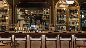 Un espace bar avec des chaises et des tables en bois, des étagères remplies de bouteilles et un comptoir.