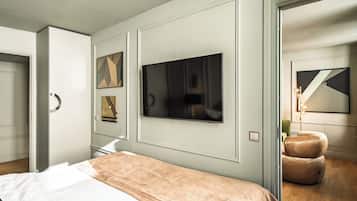 A modern bedroom with a large bed, a flat-screen TV mounted on the wall, and a seating area with a cushioned chair.