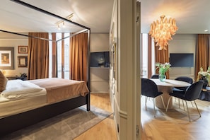 Una habitación de hotel moderna con cama con dosel, un comedor con mesa redonda y sillas, y una lámpara de araña grande.