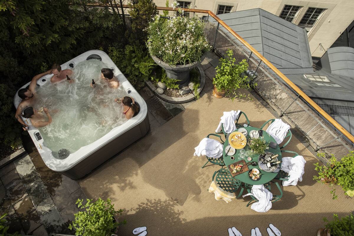 A hot tub surrounded by greenery, a dining table with chairs, and a potted plant.