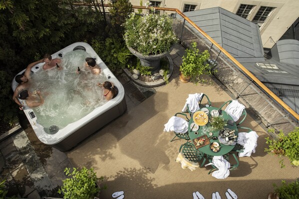 Un jacuzzi rodeado de vegetación, una mesa de comedor con sillas y una planta en maceta.