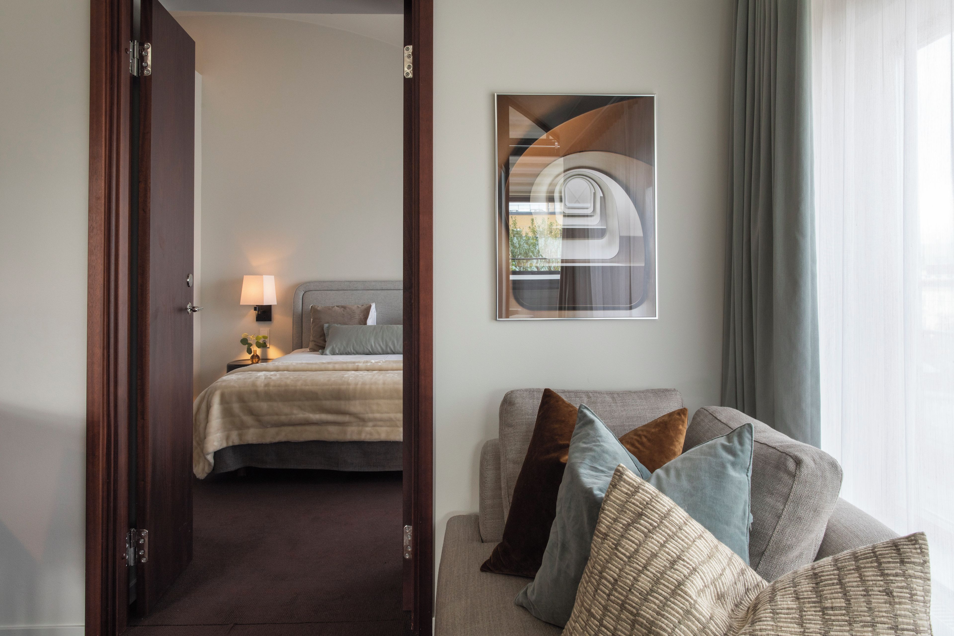 A hotel room with a bed, a bedside table with a lamp, a couch with cushions, and a painting on the wall.