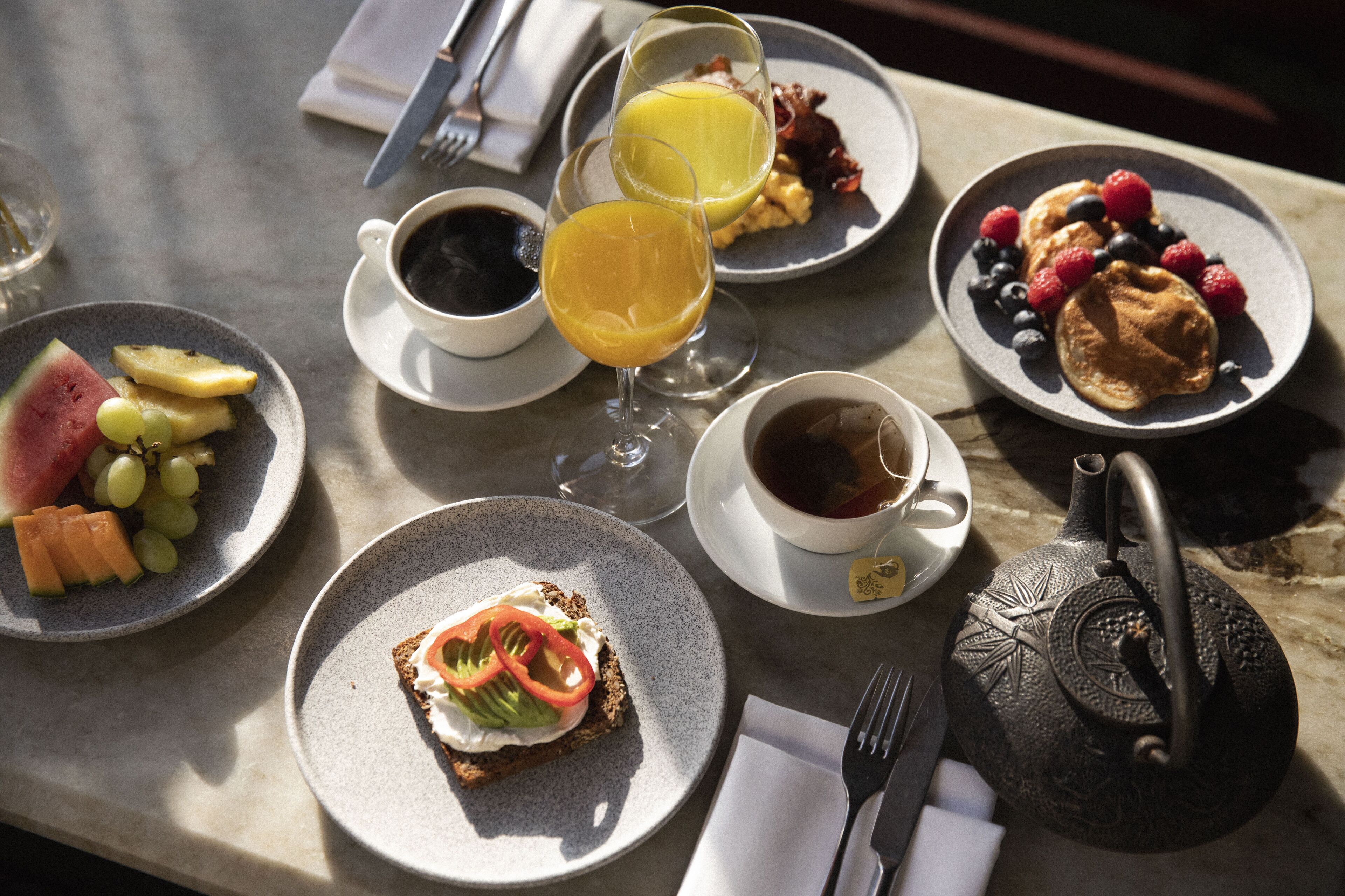 A breakfast setting with plates of food, glasses of juice, and a teapot.