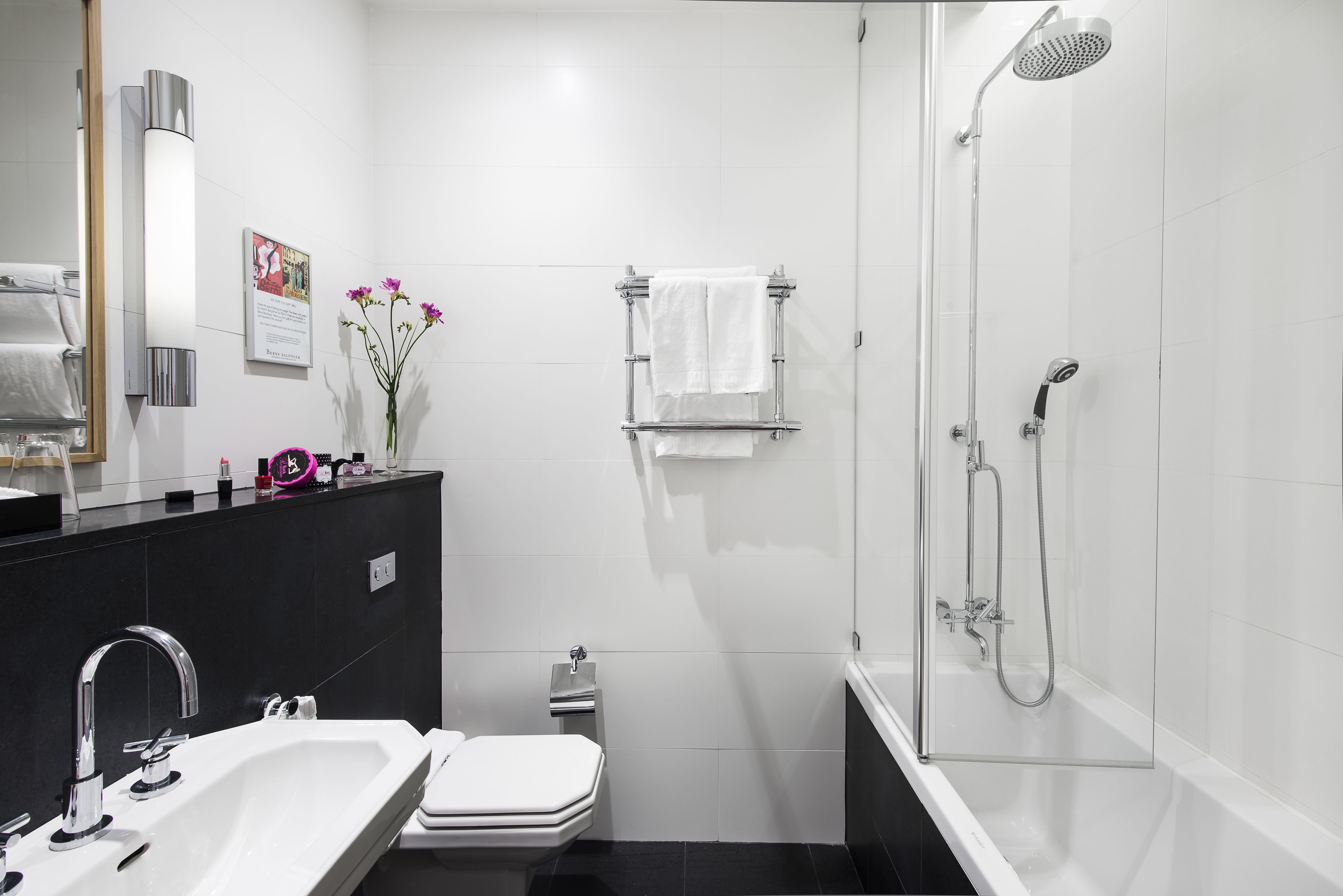 Ein modernes Badezimmer mit einem weißen Waschbecken, einer Toilette und einer Badewanne. Handtücher, ein Handtuchhalter, eine Duschbrause und ein Spiegel sind ebenfalls vorhanden.