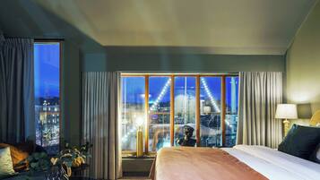 A hotel room with a large bed, a view of the cityscape through floor-to-ceiling windows, and a night sky.