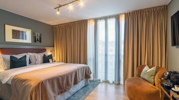 A modern hotel room with a large bed, a seating area, and a flat-screen TV.