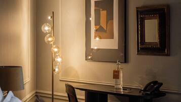 A hotel room with a bed, a desk, a chair, a lamp, and framed artwork on the wall.