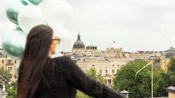 Une personne tenant des ballons sur un balcon donnant sur un bâtiment historique doté de coupoles et présentant une architecture classique.